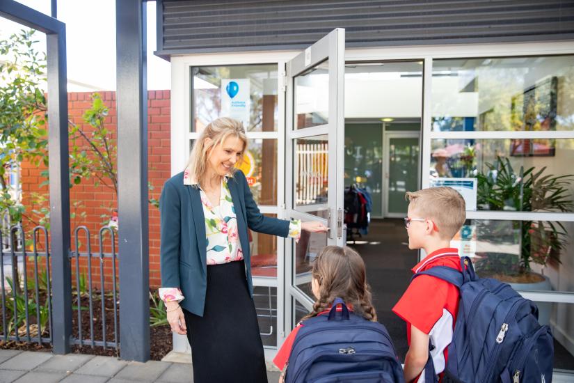 A teacher welcomes students at the school entrance door